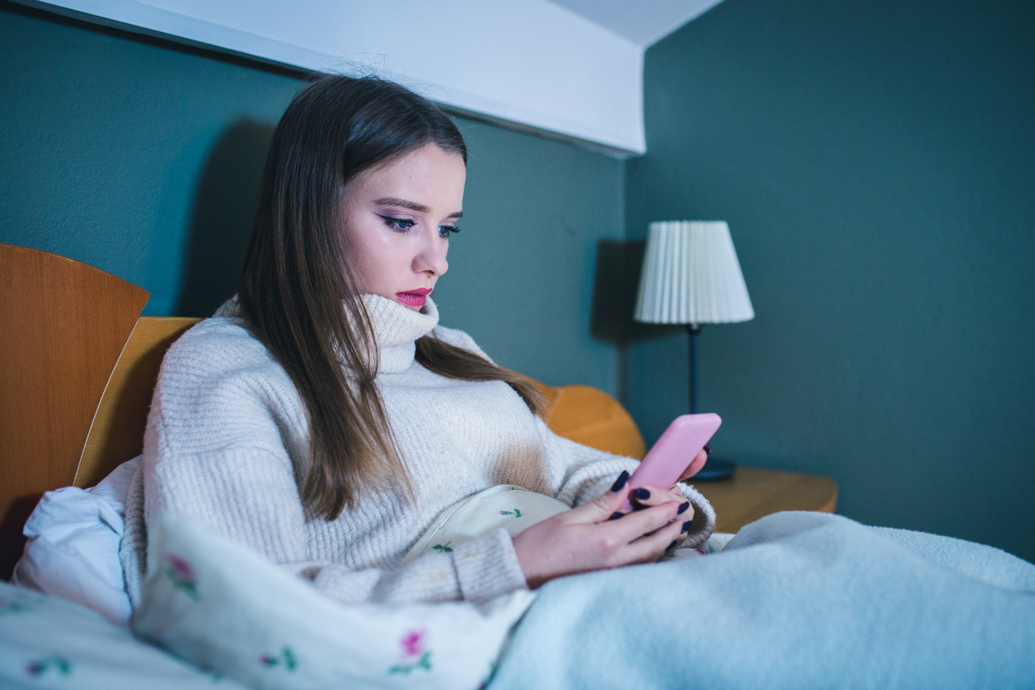 Teenager sat in bed looking at a pink smartphone