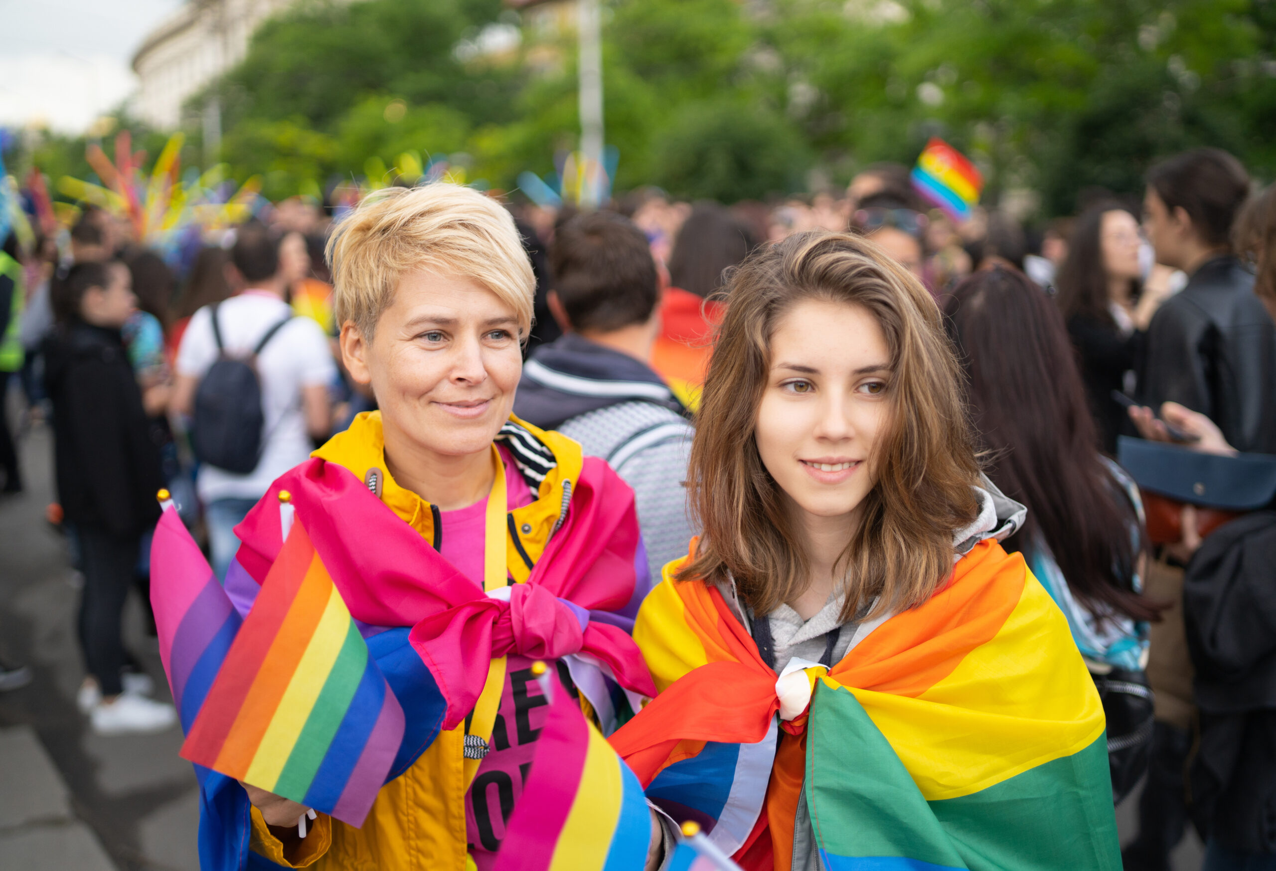 Mother and her daughter stood smiling wrapped in pride rainbow flags