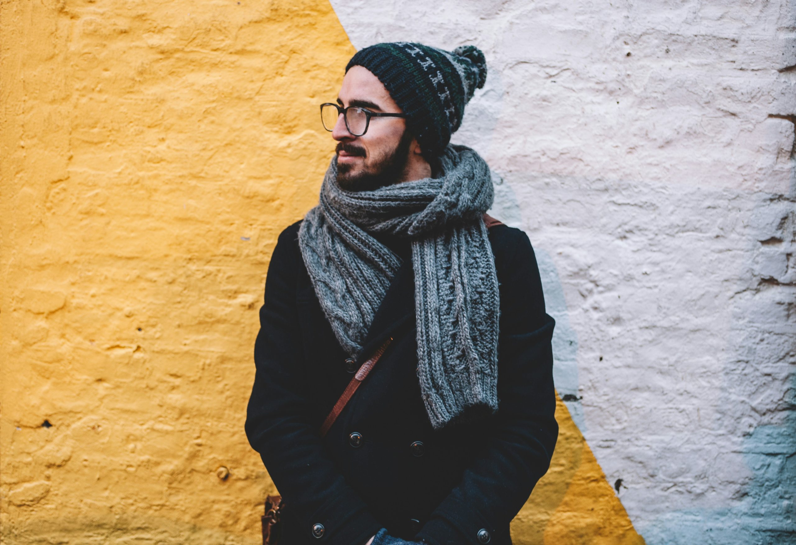 Man dressed in winter clothing with a wooly hat and scarf stood next to a bright coloured wall